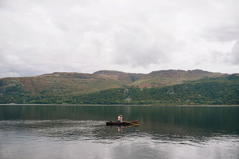 romantic photo of couple in row boat on lake with mountains in the background