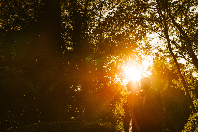 sun flare photo of couple embracing between trees