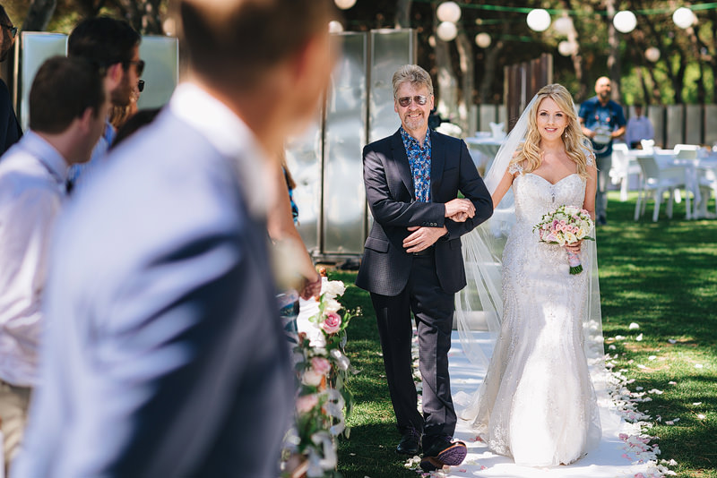 Father walks the bride down a white fabric walkway, decorated wi