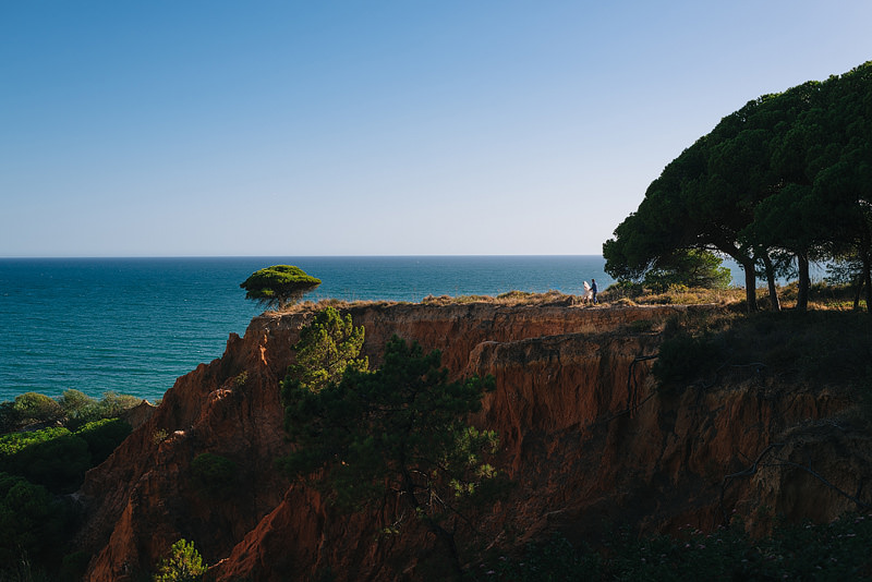bride and groom walking along an epic algarve red sand clifftop