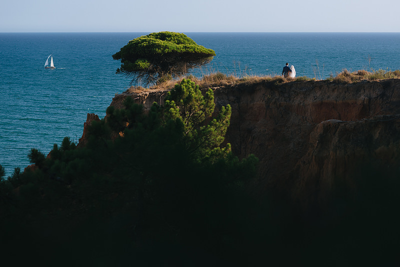 couple watching a yatch sail by from the top of a cliff