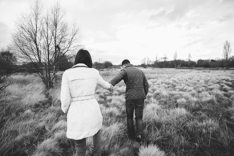 Couple walking through field hand in hand for their engagement shoot