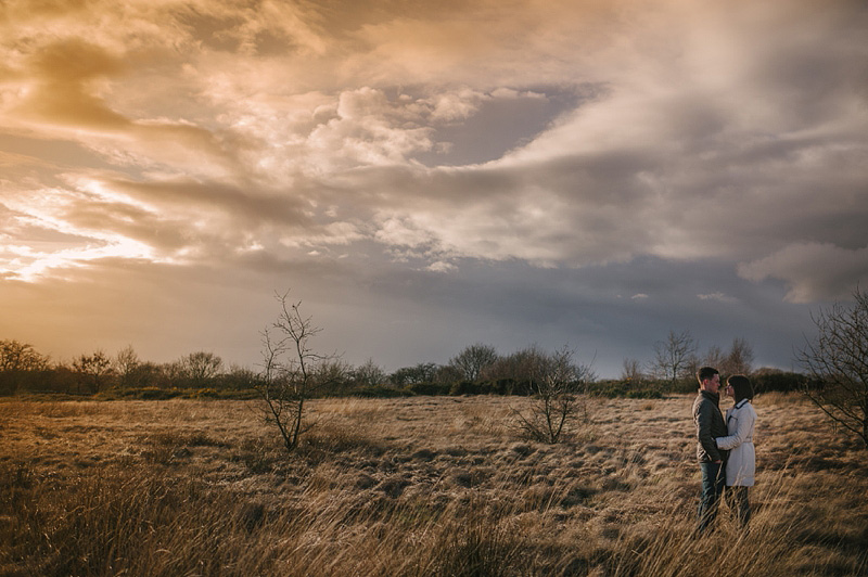 Amazing engagement photography of a couple in a fieldd underneath a dramatic stormy sky