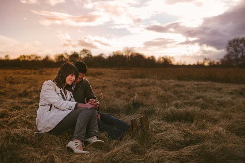 Couple sitting in a field with the sunset behind them in Pelsall